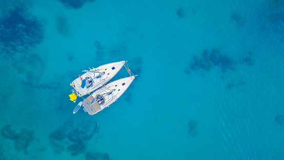 Aerial view of two sailing boats anchoring next to reef. Bird eye view, water sport theme.