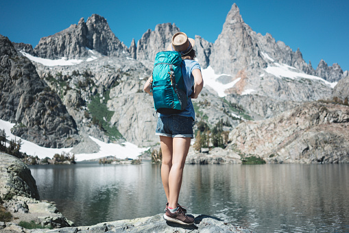 Woman backpacker traveling in the stunning mountain wilderness, standing in front of amazing cold lake