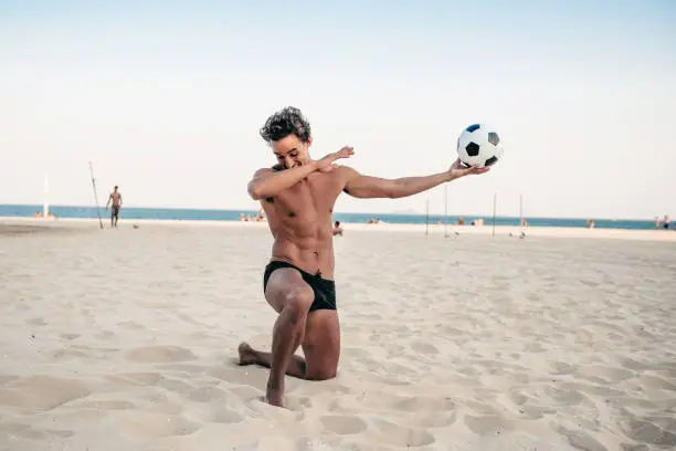 smiling handsome brazilian man on knee posing with soccerball at beach in Rio de Janeiro