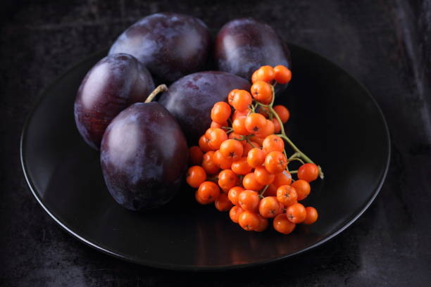 istock Blue plums and orange rowan berries on a black plate for designer 850183512
