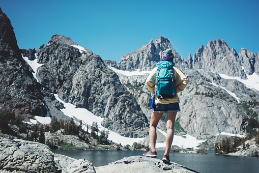 Young woman with backpack traveling in snow mountain wilderness. Hipster hiking near stunning ice lake