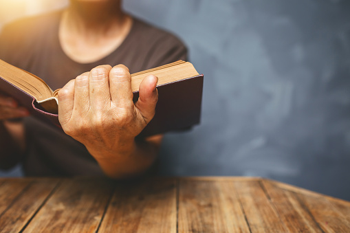 Senior woman reading a book at living room with old vintage table and concrete wall background.