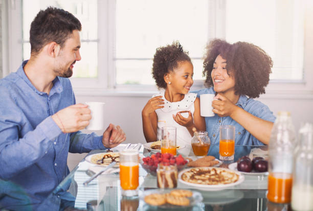 foto di una giovane famiglia felice che sta facendo colazione - women juice drinking breakfast foto e immagini stock