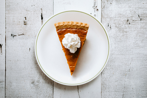 A high angle view looking down on a slice of freshly baked pumpkin pie, just in time for your autumn or Thanksgiving season celebration.  Horizontal image with copy space.