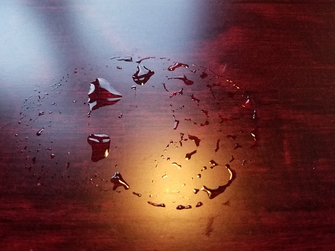 some water drips from a glass on a dark wood table