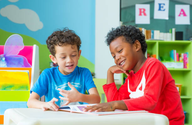 dwa dziecko chłopiec siedzieć na stole i czytanie książki w bibliotece przedszkolnej, przedszkole koncepcji edukacji szkolnej - child at library zdjęcia i obrazy z banku zdjęć
