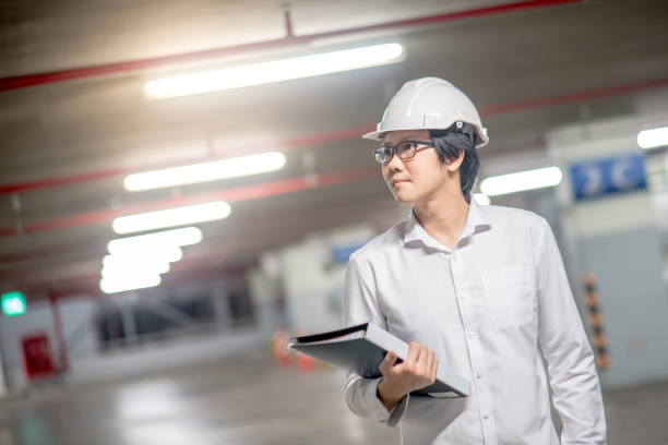 Young Asian Engineer or Architect holding files while wearing personal protective equipment safety helmet at construction site