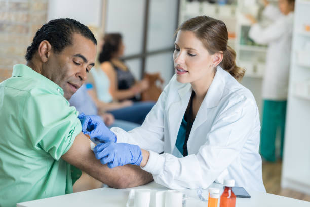 Caring healthcare professional places bandage on man's arm Confident mid adult Caucasian female healthcare professional gently places a bandage on a mature male patient's arm. The patient received a flu or other preventative vaccine. flu vaccine photos stock pictures, royalty-free photos & images