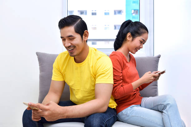 Young asian couple sitting on the sofa with mobile phone Young asian couple sitting on the sofa with mobile phone at apartment malay couple stock pictures, royalty-free photos & images