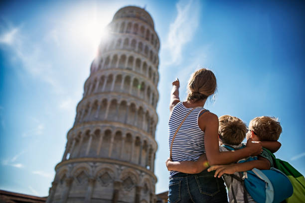 Tourists kids sightseeing Pisa, Italy. Brothers and sister are standing in the Piazza del Miracoli amd admiring the famous leaning tower of Pisa.\n\n