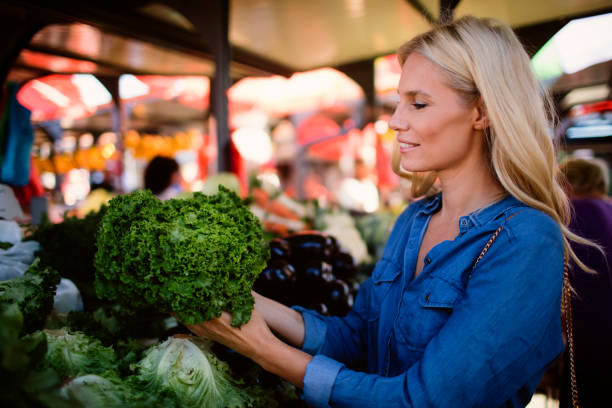 Mid adult woman buying vegetables on greenmarket. She is choosing green salad