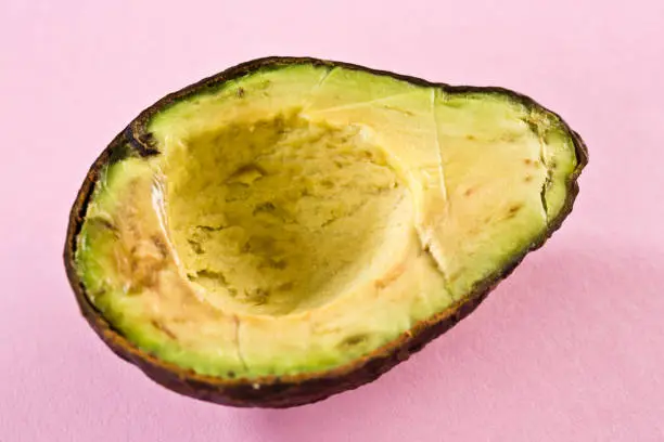 An avocado pear has been sliced in half, revealing a brownish, rotting interior.