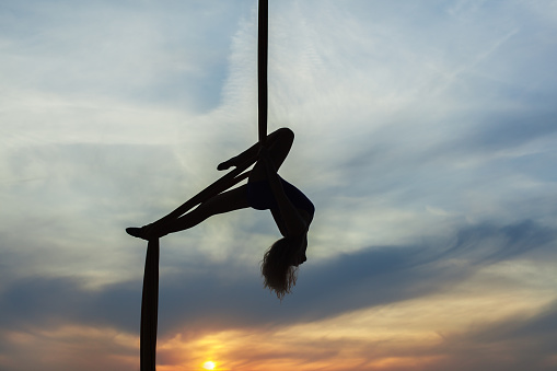 Woman's equilibrist does tricks high in the sky in the setting sun. Only the contours of the athlete.