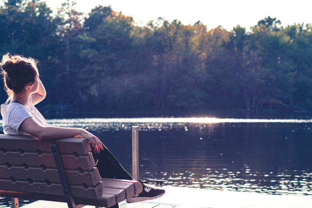 Young female student taking a seat and admiring the still waters of the lake after a workout