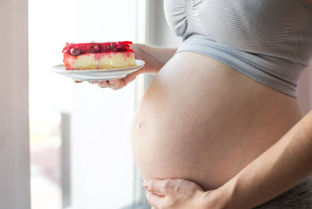 A pregnant woman with belly holding a piece of cheesecake. Concept weight control and an unhealthy diet during pregnancy stock photo