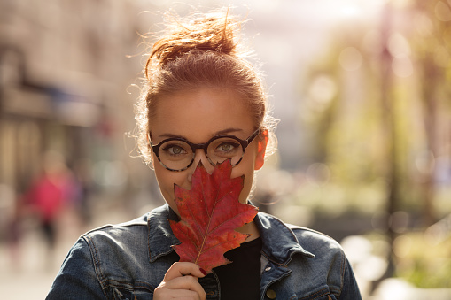 Beautiful woman holding autumn leaf on the street. Autumn concept.