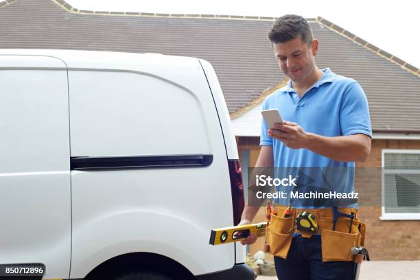 Builder With Van Texting On Mobile Phone Outside House Stock Photo - Download Image Now