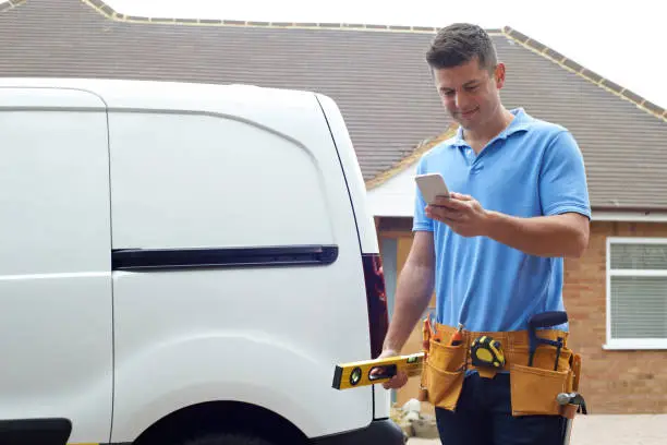 Builder With Van Texting On Mobile Phone Outside House