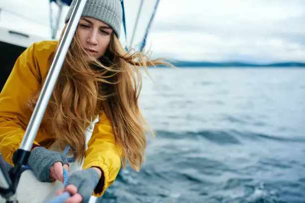 Young woman pulling yacht rope while sailing on a windy gloomy day