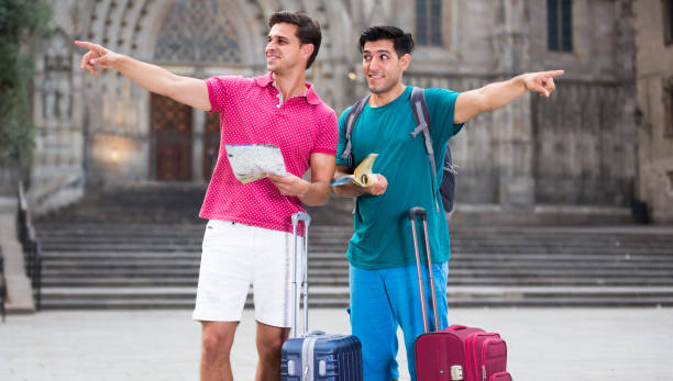 Two friends tourists with suitcases are walking with map and guide-book on the street in Barcelona.