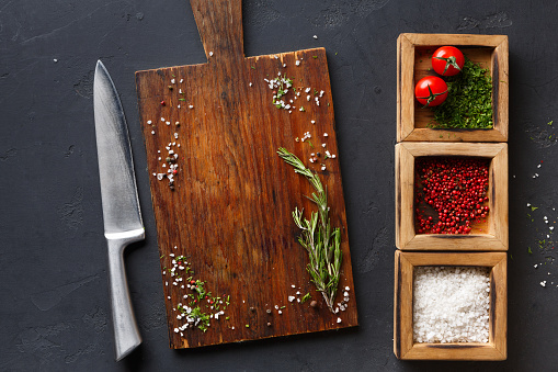 Wooden desk with spices assortment, salt, peppers and parsley in wooden boxes on dark background, top view, copy space.