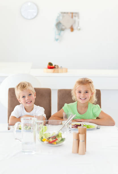 adorables hermanos comiendo una ensalada juntos en la cocina - 46334 fotografías e imágenes de stock