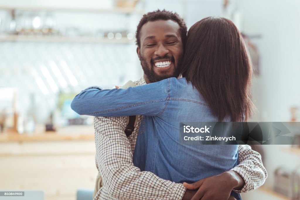 Happy man hugging his best friend in coffeehouse Long-awaited meeting. Charming young man hugging his best friend having met her in the coffeehouse after a long period without seeing each other Reunion - Social Gathering Stock Photo