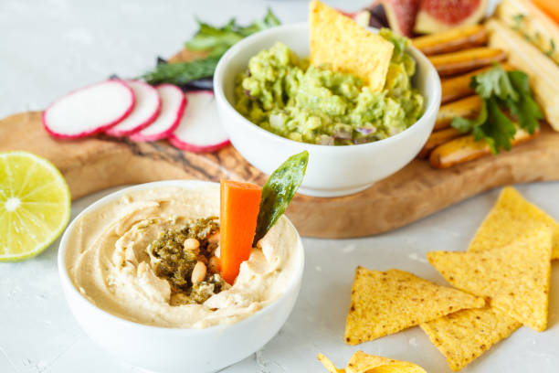 Hummus and guacamole with vegetables and snacks on a wooden board stock photo