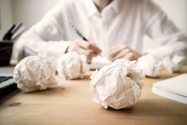 Crumpled papers and overwork this photo is a front view of crumpled papers on the desk and a working man crumpled paper ball stock pictures, royalty-free photos & images