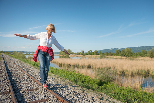 Happy smiling old woman balancing with arms wide open on the rails. Concept: active seniors, vitality