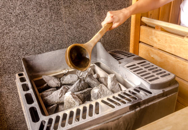 Woman is pouring water into hot stone in Sauna spa room stock photo