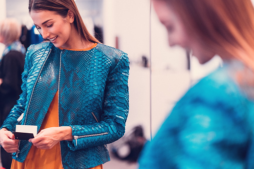 Young woman in front of the mirror looking at the price tag of a new jacket