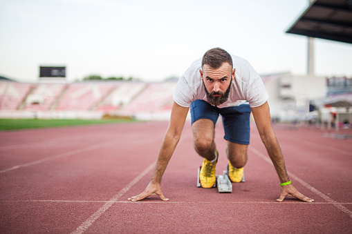 Focused young professional male Caucasian athlete ready for the run race in a sprint starting position