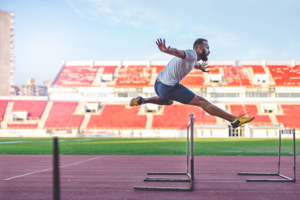 Hurdling 35 years old man at the stadium. He is jumping over the hurdle, and improving his jumping skills hurdle stock pictures, royalty-free photos & images