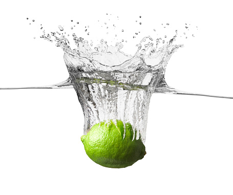 One fresh green juicy lime is falling into crystal clear water. There are splashes of water and bubbles rising high above the lime from where it broke the waters surface. The fruit and splashes are isolated on a white background with a clipping path.