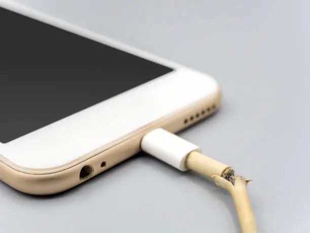 Close-up image of damaged charger cable connecting with smartphone on gray background