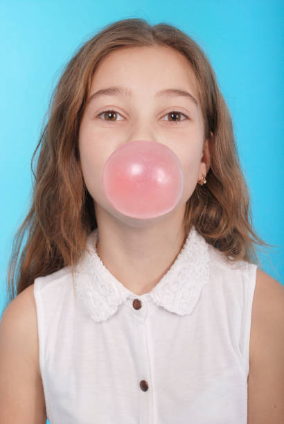 Girl blowing a big bubble gum bubble isolated on blue
