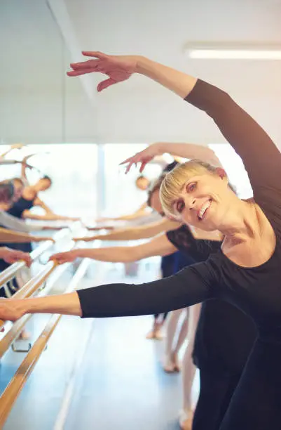 Photo of Smiling adult woman stretching and doing gymnastics in ballet class