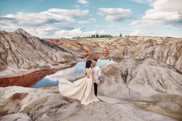 couple stands on the precipice of the mountain and the red lake and hugging. the bride and groom in love, the woman in long dress in the arms of men - long hair red hair women men imagens e fotografias de stock