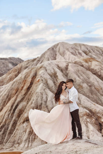 couple stands on the precipice of the mountain and the red lake and hugging. the bride and groom in love, the woman in long dress in the arms of men - long hair red hair women men imagens e fotografias de stock