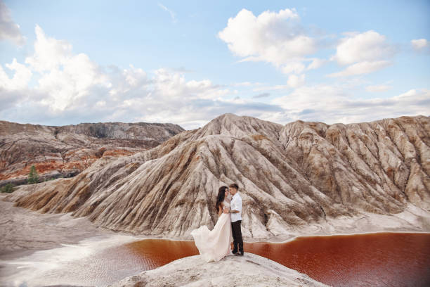 couple stands on the precipice of the mountain and the red lake and hugging. the bride and groom in love, the woman in long dress in the arms of men - long hair red hair women men imagens e fotografias de stock