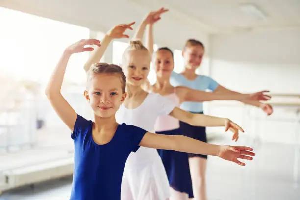 Young little cheerful girls performing ballet and smiling looking at camera in the class.