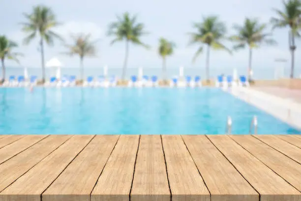 Photo of Empty wooden table in front with blurred background of swimming pool at beach,space for montage products