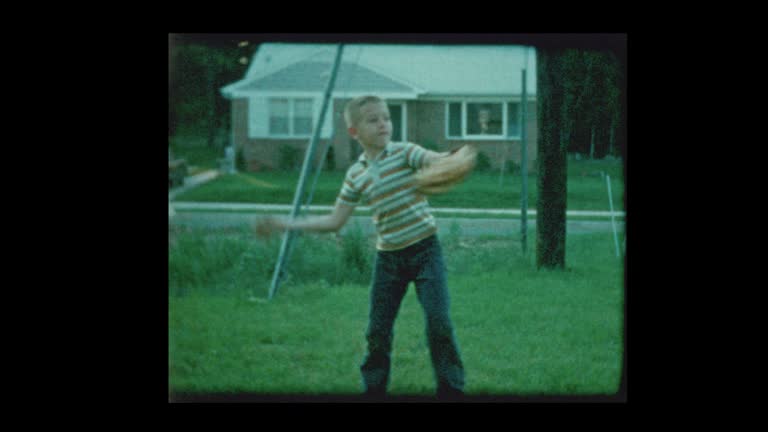 Young boy playing catch with baseball in suburban backyard 1960