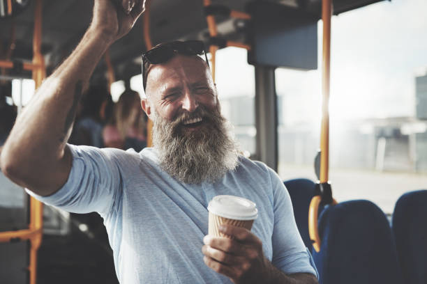 homme d’âge mûr souriant avec une barbe et un café dans le bus - coffee to go flash photos et images de collection