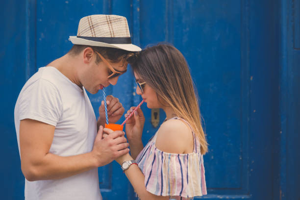 Young modern couple in love drinking juice from the same glass outdoor. Space for copy.