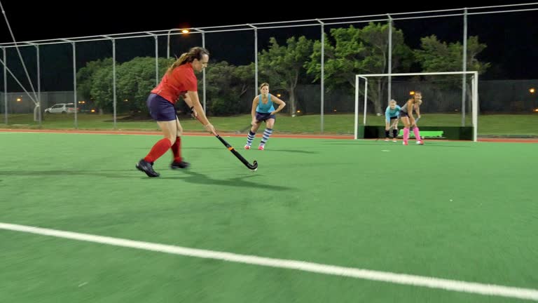 Young female field hockey players playing on field, taking a shot and scoring goal