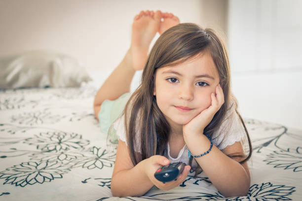 istock Little girl watching TV lying on bed with remote control in hand 851003620