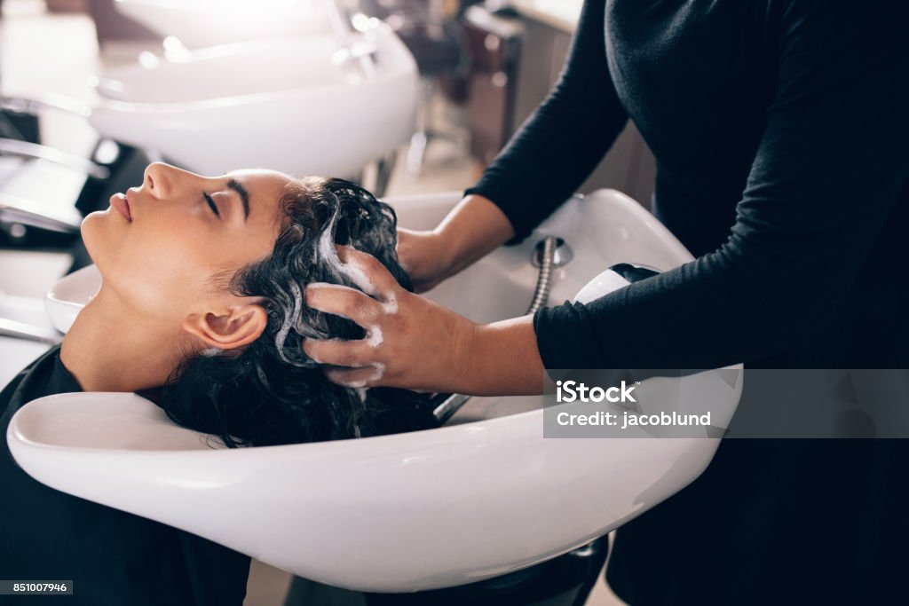 Woman getting hair shampooed at salon Woman applying shampoo and massaging hair of a customer. Woman having her hair washed in a hairdressing salon. Hair Salon Stock Photo