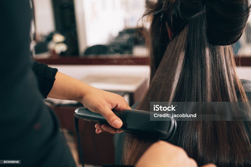 Woman at the hair salon getting her hair styled Hairdresser using a hair straightened to straighten the hair. Hair stylist working on a woman's hair style at salon. Hair Stock Photo